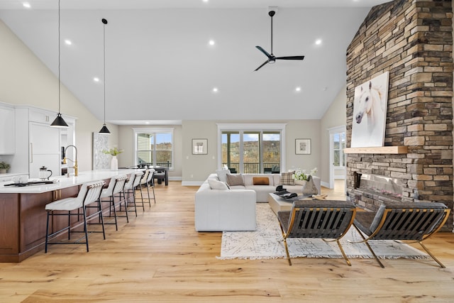 living room featuring ceiling fan, a stone fireplace, a wealth of natural light, and light hardwood / wood-style floors