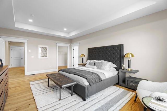 bedroom featuring a closet, a walk in closet, light hardwood / wood-style floors, and a tray ceiling