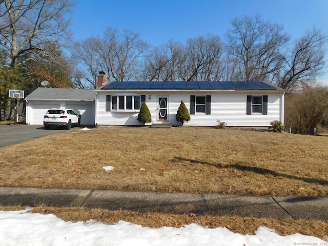 ranch-style home featuring an attached garage, a front lawn, roof mounted solar panels, a chimney, and driveway