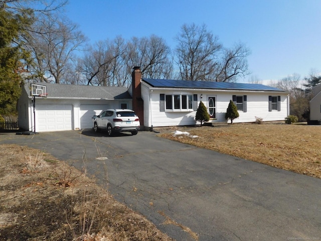 single story home with solar panels, a front lawn, a chimney, a garage, and driveway