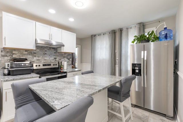 kitchen with white cabinetry, light stone countertops, appliances with stainless steel finishes, and a breakfast bar area