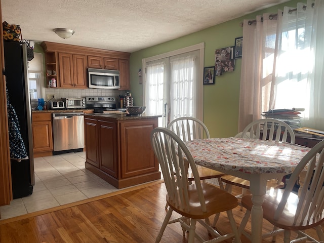 kitchen featuring stainless steel appliances, backsplash, dark stone countertops, light hardwood / wood-style floors, and a textured ceiling