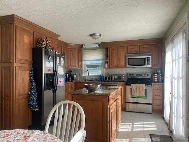 kitchen featuring sink, light tile patterned floors, dark stone counters, a kitchen island, and appliances with stainless steel finishes