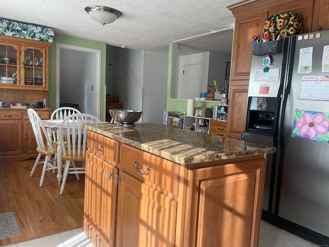 kitchen featuring stainless steel fridge, light wood-type flooring, dark stone counters, a textured ceiling, and a center island