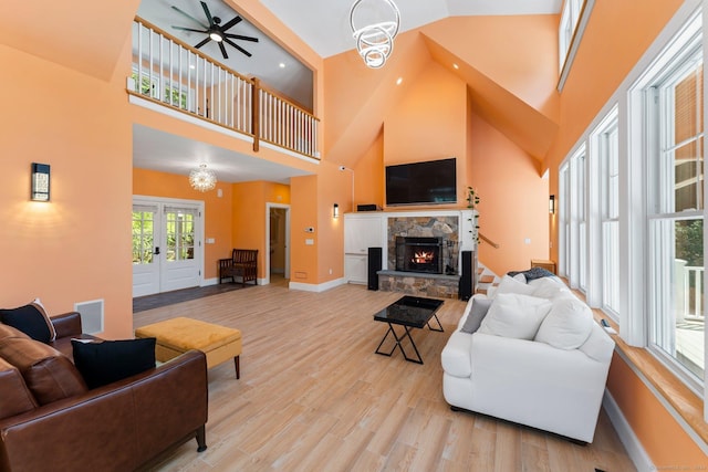 living area featuring a stone fireplace, a high ceiling, visible vents, baseboards, and light wood-style floors