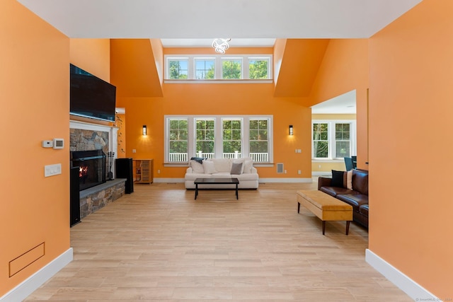 living room featuring a high ceiling, baseboards, a fireplace, and light wood finished floors