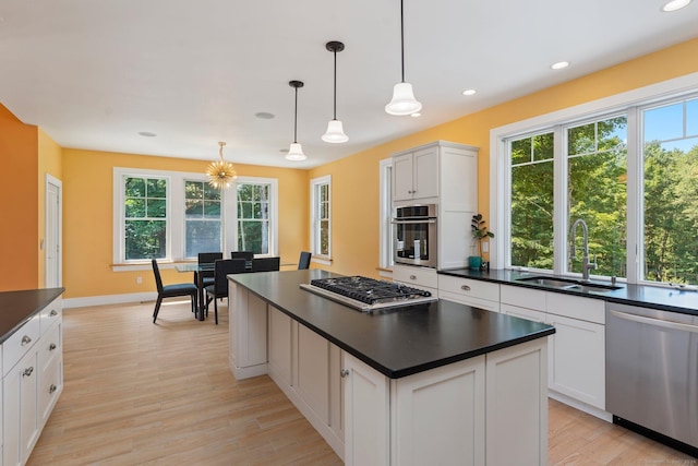 kitchen featuring dark countertops, hanging light fixtures, appliances with stainless steel finishes, white cabinets, and a sink