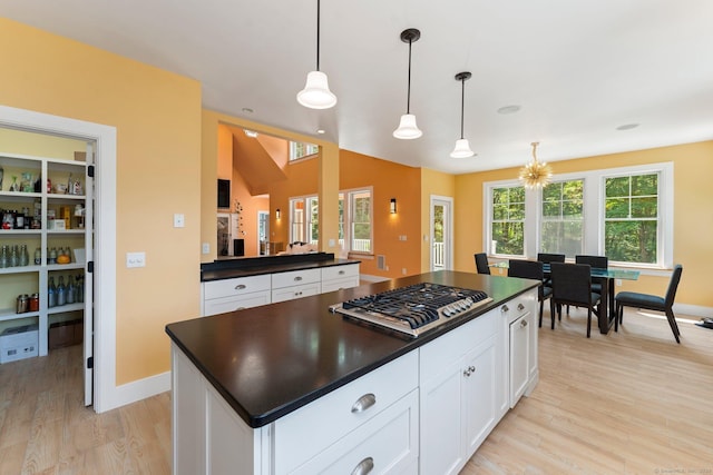 kitchen with stainless steel gas cooktop, white cabinets, light wood finished floors, dark countertops, and pendant lighting