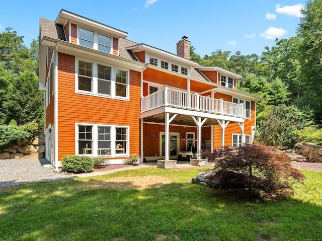 rear view of property with a chimney, a patio area, a yard, and a balcony