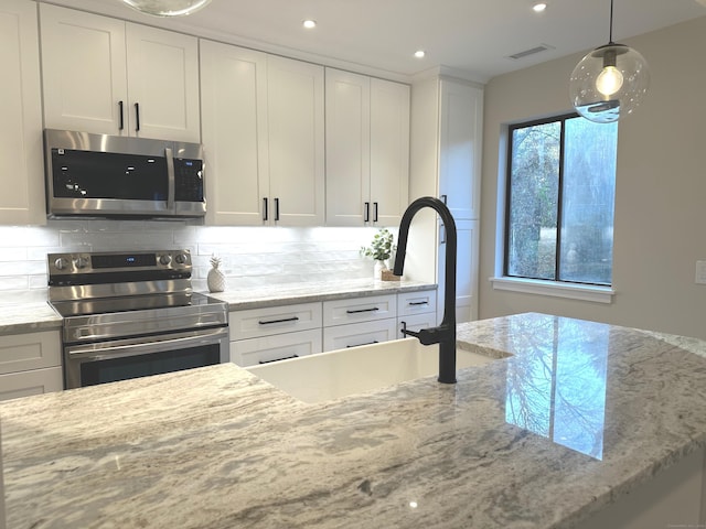 kitchen featuring pendant lighting, backsplash, light stone counters, white cabinetry, and stainless steel appliances