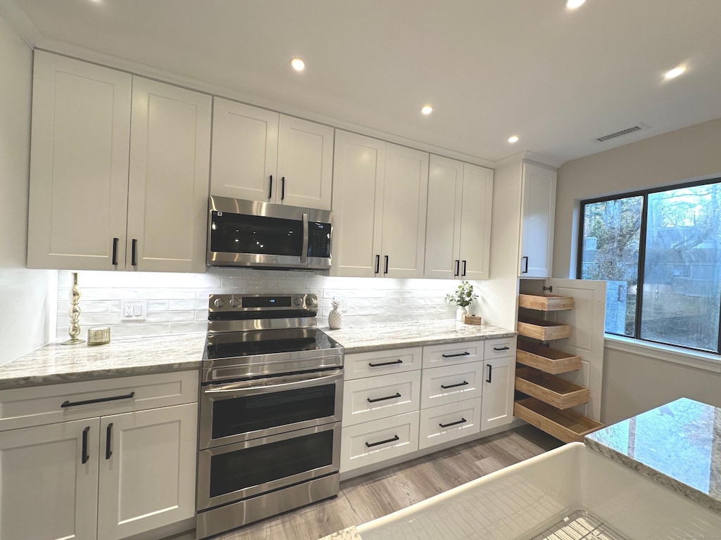 kitchen featuring light hardwood / wood-style flooring, light stone countertops, appliances with stainless steel finishes, tasteful backsplash, and white cabinetry