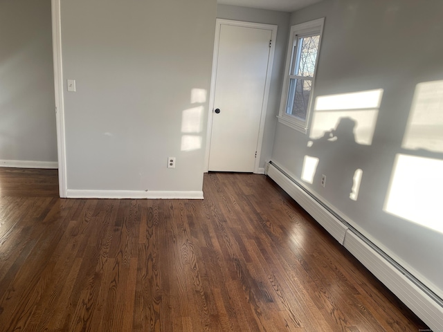 empty room with dark hardwood / wood-style floors and a baseboard heating unit