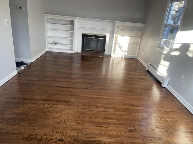 unfurnished living room with a tile fireplace, dark hardwood / wood-style flooring, a baseboard radiator, and built in features