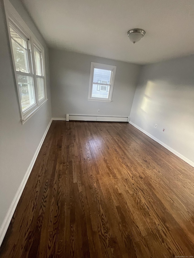 unfurnished room featuring a healthy amount of sunlight, dark hardwood / wood-style floors, and a baseboard heating unit