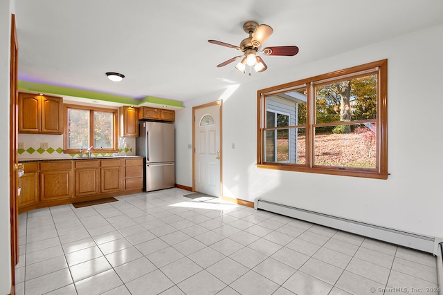 kitchen featuring baseboard heating, backsplash, stainless steel fridge, light tile patterned flooring, and ceiling fan