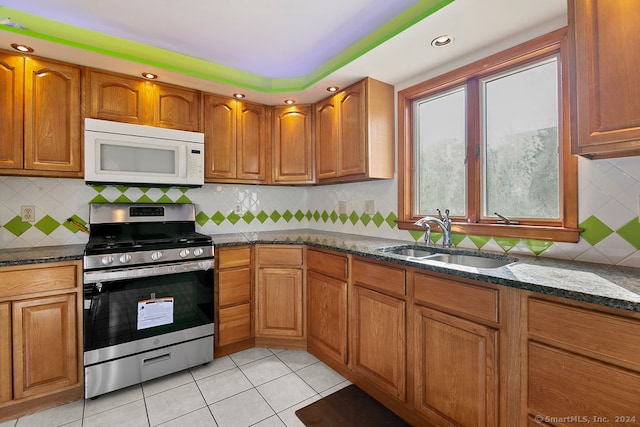 kitchen with tasteful backsplash, light tile patterned flooring, sink, dark stone counters, and stainless steel stove