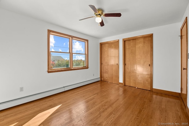 unfurnished bedroom with ceiling fan, multiple closets, a baseboard heating unit, and light wood-type flooring