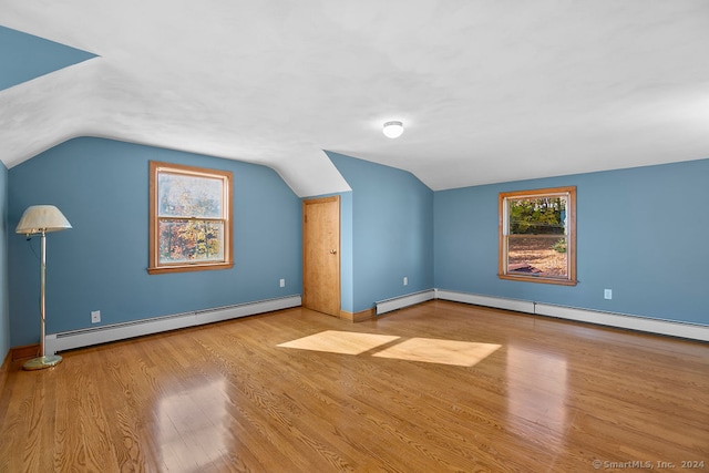 additional living space with vaulted ceiling, a baseboard heating unit, and light hardwood / wood-style floors