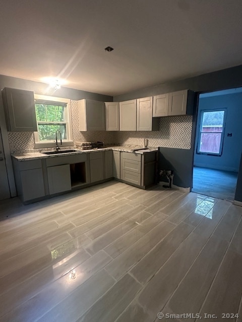 kitchen featuring light hardwood / wood-style floors, decorative backsplash, sink, and gray cabinetry