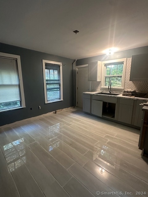 kitchen with gray cabinets, sink, light wood-type flooring, and backsplash