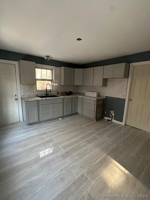 kitchen with gray cabinets, sink, light wood-type flooring, and decorative backsplash