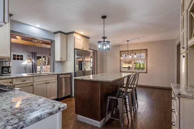 kitchen with appliances with stainless steel finishes, a kitchen island, dark hardwood / wood-style flooring, pendant lighting, and light stone counters