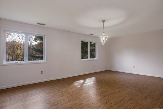 spare room with a notable chandelier and dark hardwood / wood-style floors