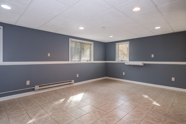 basement with a paneled ceiling, light tile patterned flooring, and a baseboard radiator