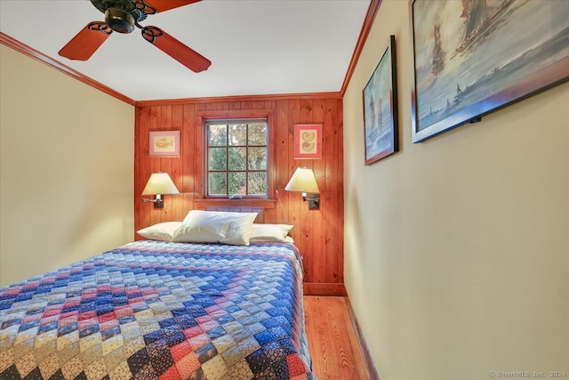 bedroom featuring ceiling fan, crown molding, light hardwood / wood-style flooring, and wooden walls