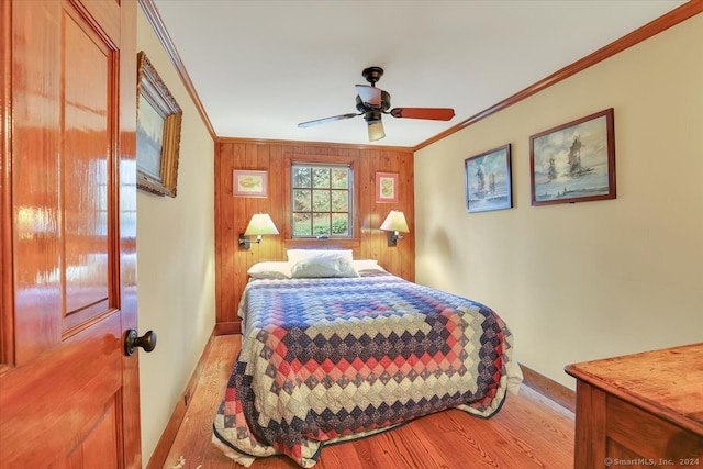 bedroom featuring ceiling fan, wood walls, ornamental molding, and light hardwood / wood-style flooring