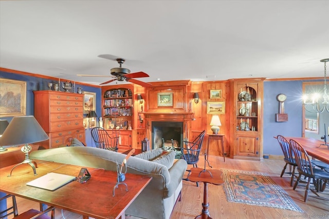 living room with ceiling fan with notable chandelier, ornamental molding, light wood-type flooring, and a fireplace