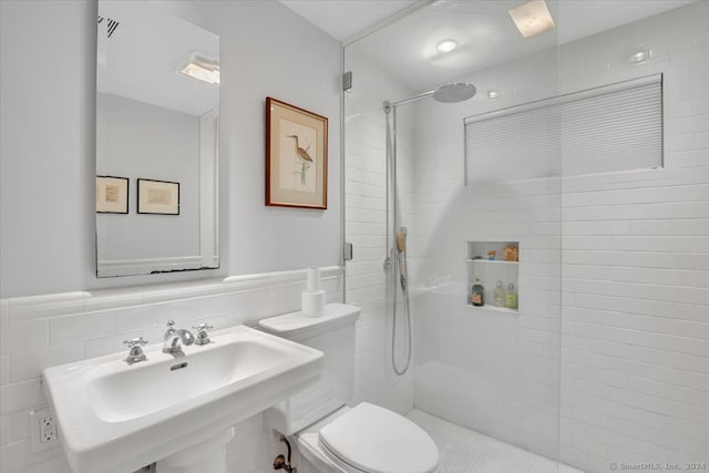 bathroom with tile walls, sink, a tile shower, and toilet