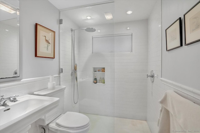 bathroom with tile walls, tiled shower, sink, and toilet