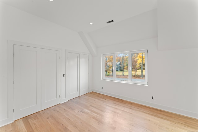 unfurnished bedroom featuring lofted ceiling, light hardwood / wood-style flooring, and two closets