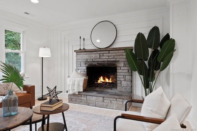 living room featuring a stone fireplace, wood-type flooring, and crown molding