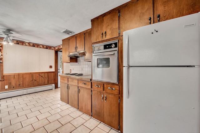 kitchen featuring white appliances, a textured ceiling, a baseboard radiator, wooden walls, and ceiling fan