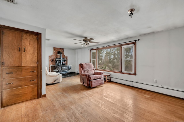 living area with ceiling fan, a baseboard heating unit, light hardwood / wood-style flooring, and a wood stove