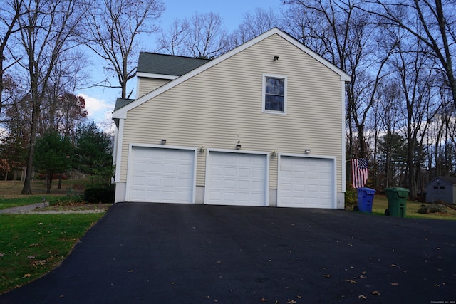 view of side of property with aphalt driveway, an attached garage, and a shingled roof