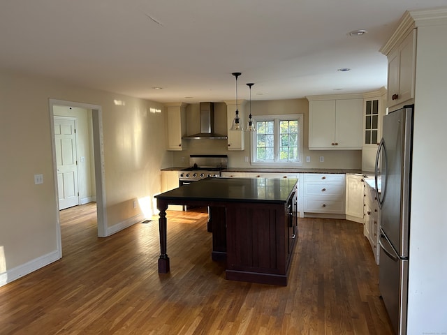 kitchen with wall chimney range hood, a kitchen island, hanging light fixtures, stainless steel appliances, and dark hardwood / wood-style floors