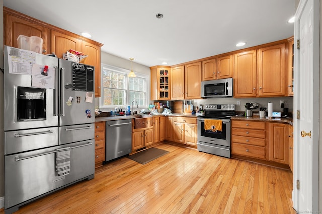 kitchen featuring sink, appliances with stainless steel finishes, decorative light fixtures, and light wood-type flooring