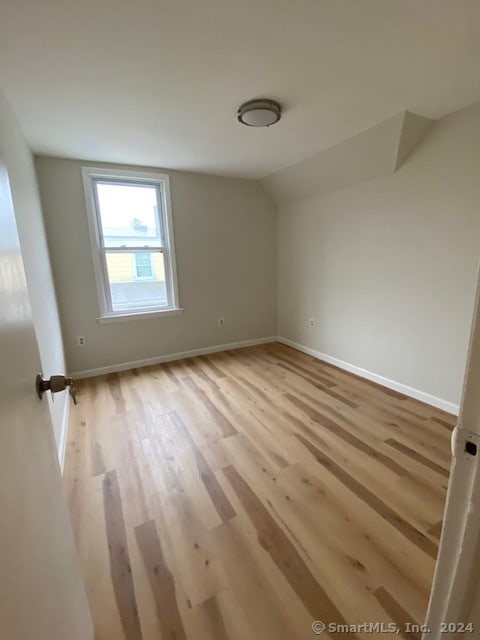 spare room with light hardwood / wood-style flooring and vaulted ceiling