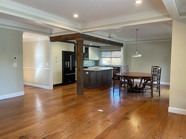 kitchen featuring hardwood / wood-style flooring, ornamental molding, decorative light fixtures, black fridge with ice dispenser, and white cabinetry