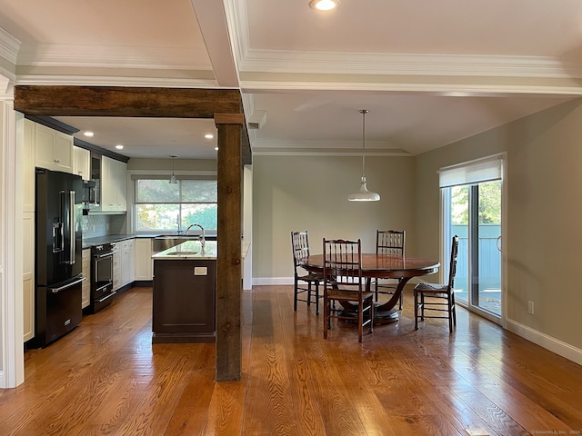 dining room with ornamental molding, a healthy amount of sunlight, beamed ceiling, and dark hardwood / wood-style flooring