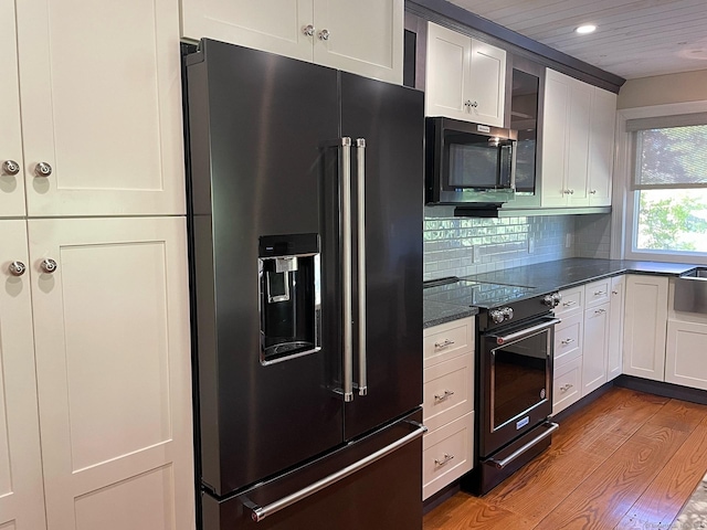 kitchen featuring tasteful backsplash, glass insert cabinets, dark stone counters, white cabinets, and black appliances