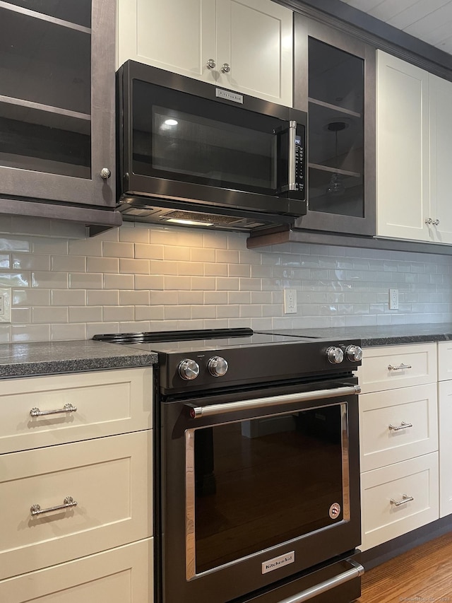 kitchen with electric range oven, white cabinets, wood finished floors, and decorative backsplash