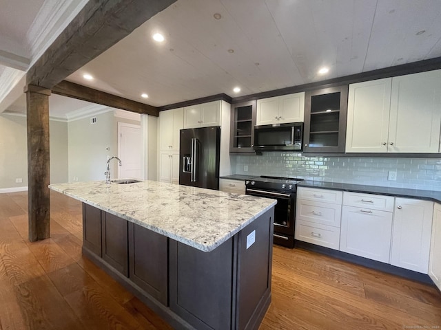 kitchen featuring tasteful backsplash, an island with sink, black appliances, a sink, and dark wood-type flooring