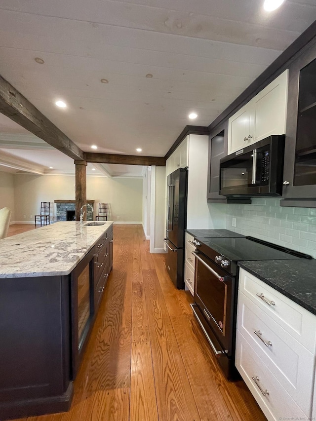kitchen with wood finished floors, glass insert cabinets, light stone counters, decorative columns, and black appliances