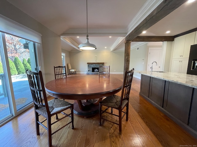 dining space featuring beamed ceiling, ornamental molding, hardwood / wood-style floors, sink, and a fireplace