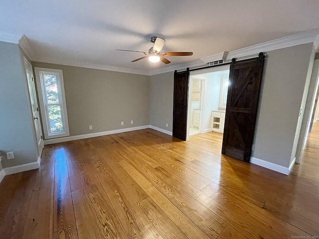 empty room with light wood-style flooring, a barn door, baseboards, ornamental molding, and a ceiling fan