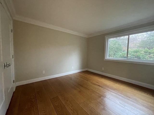 empty room featuring hardwood / wood-style flooring, ornamental molding, and baseboards